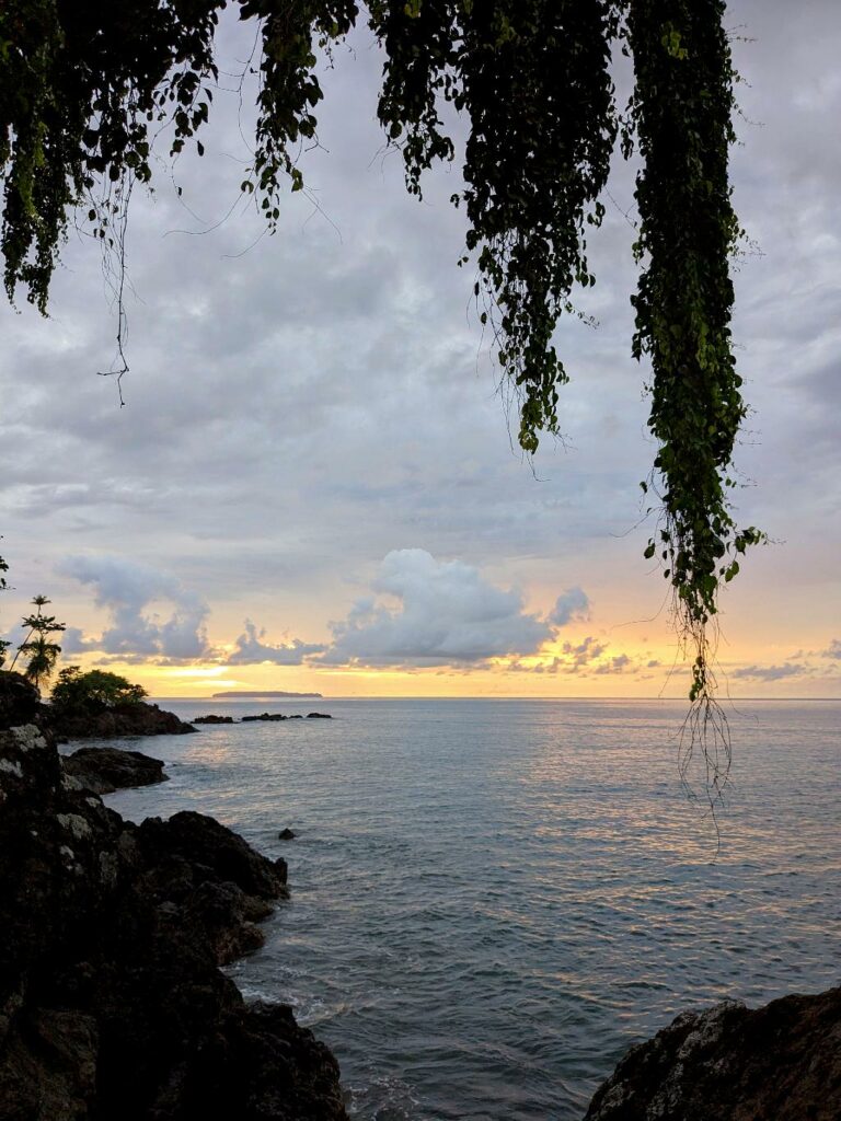 View of the sunset over the Pacific Ocean with Caño Island in the distance, as seen from a rocky beach