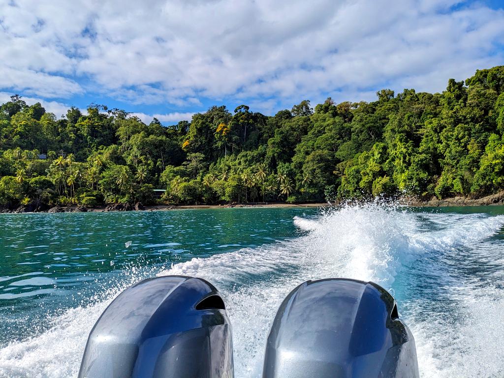 A picture taken from a boat featuring the boat's engines, the blue ocean, and the verdant jungle