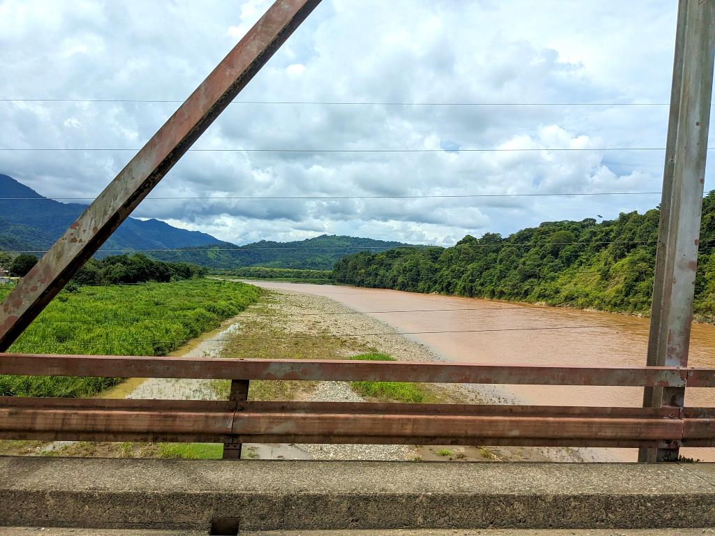 A bridge spanning a long, flat river nestled amidst a forest near the ocean