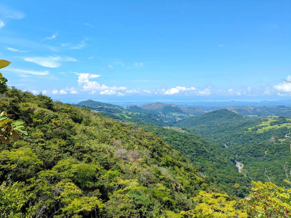 Panoramic view of verdant hills surrounding the Aranjuez River, with the distant ocean meeting the blue sky.