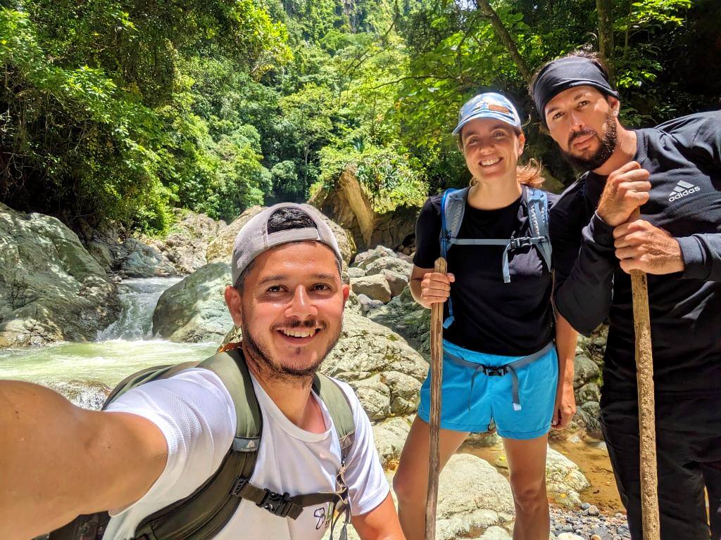Hikers alongside a local baquiano guide with the Aranjuez River in the backdrop during the Boquerones Hike, Bajo Caliente, Puntarenas.