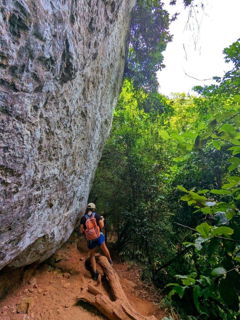 Hiker navigating the El Encanto trail beside a prominent rounded boulder.