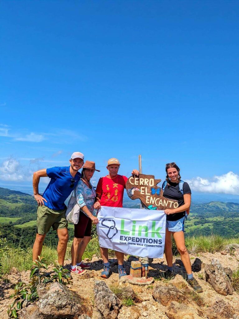 Hikers displaying the 'Link Expeditions' flag beside the 'Cerro El Encanto' trail signpost.