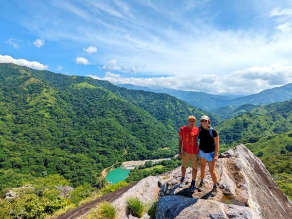 Two hikers atop a towering rock with a panoramic view of El Encanto Hydroelectric dam to the north.