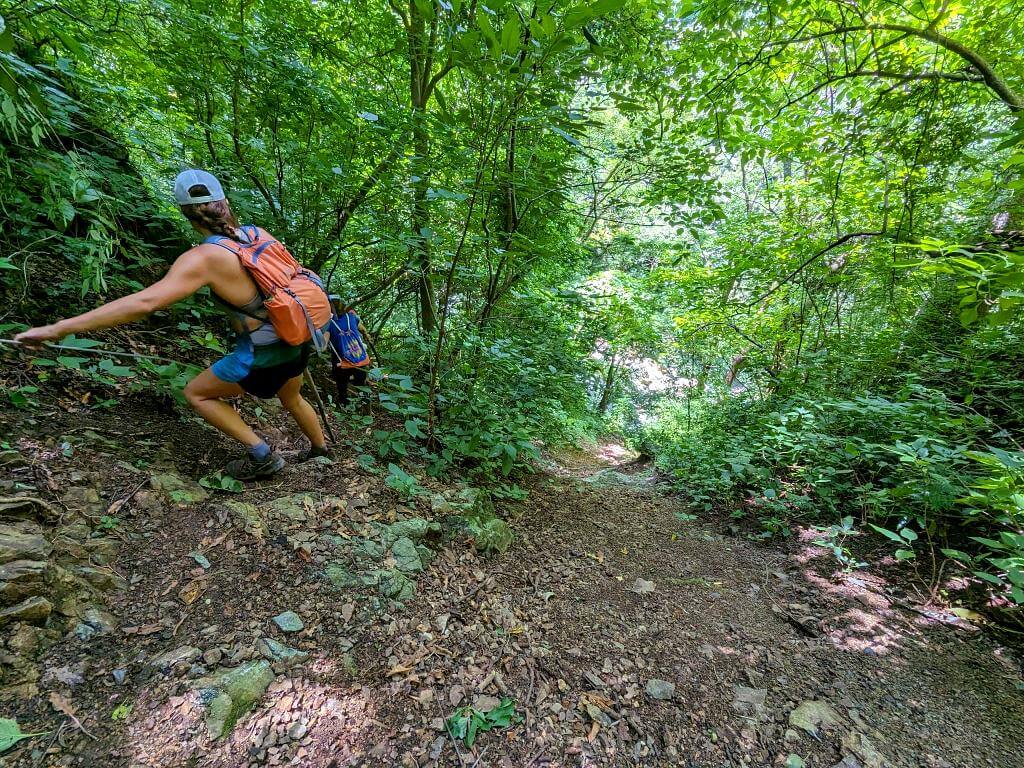 Hiker cautiously navigating a narrow trail alongside a cliff leading to the Aranjuez River during the Boquerones Hike, Bajo Caliente, Puntarenas.