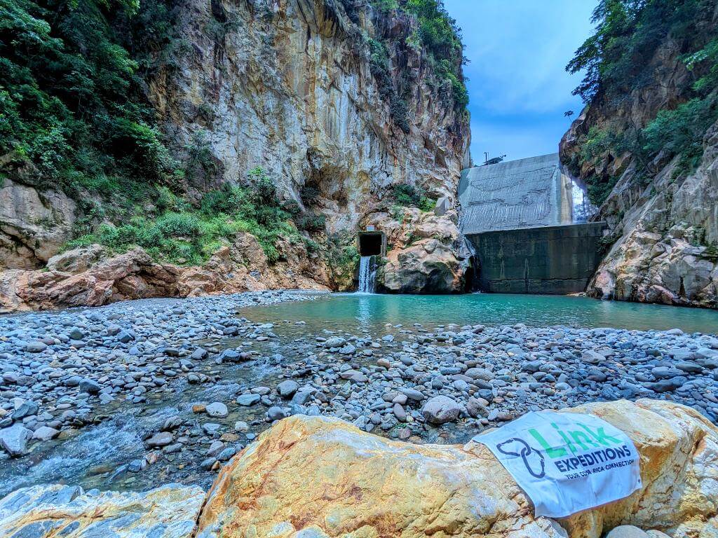 Panoramic view of the El Encanto Hydroelectric dam showcasing its turquoise natural pool, adjacent artificial waterfall, and surrounding rock formations.