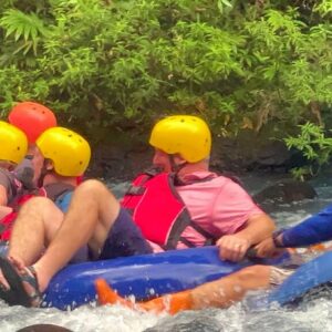 Four people float and smile down Class I & II rapids on Rio Celeste, followed by their tour guide.