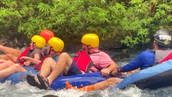 Four people float and smile down Class I & II rapids on Rio Celeste, followed by their tour guide.