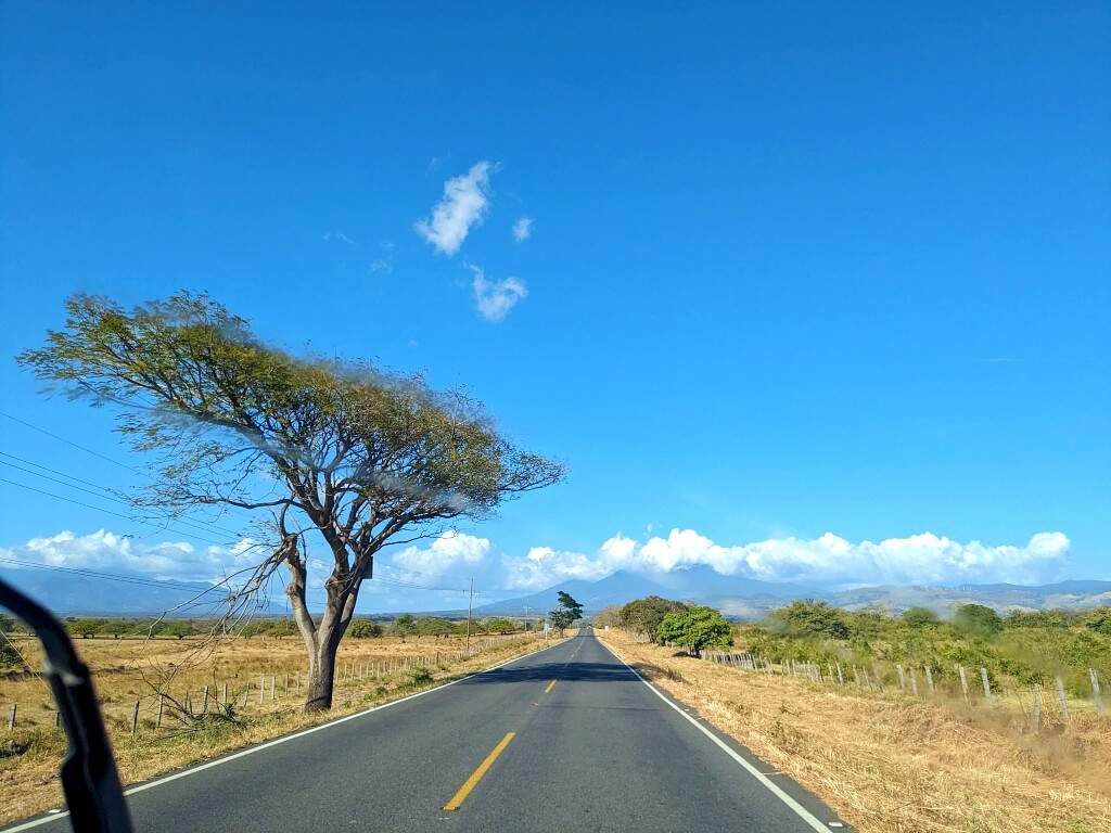 Scenic view of straight narrow paved roads leading to Bijagua with ranches and Tenorio and Miravalles volcanoes in the distance