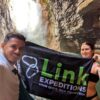 Alberto, owner of the agency, holding a banner with the company's logo in front of the blue water river and waterfalls.