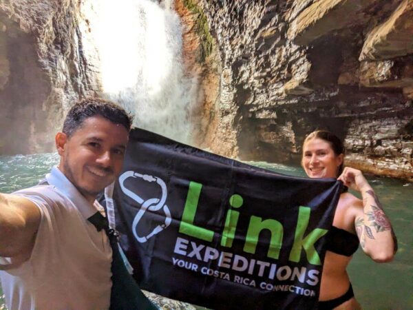 Alberto, owner of the agency, holding a banner with the company's logo in front of the blue water river and waterfalls.