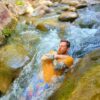Young man lying in the water enjoying sliding down a natural slide.