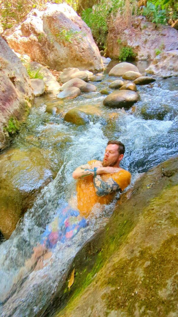Young man lying in the water enjoying sliding down a natural slide.