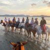 Group hanging out on the beach, waiting to start their horseback riding tour, with a sense of tranquility in the air.