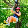 Client smiling as she slides down the canopy line, equipped with the necessary safety equipment.