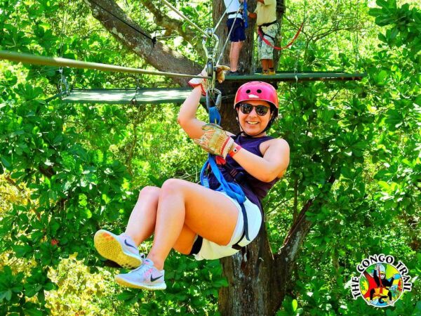 Client smiling as she slides down the canopy line, equipped with the necessary safety equipment.