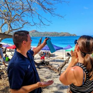 Two people talking about the natural beauty with the beach and tourists relaxing in the background.