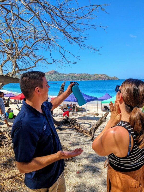 Two people talking about the natural beauty with the beach and tourists relaxing in the background.