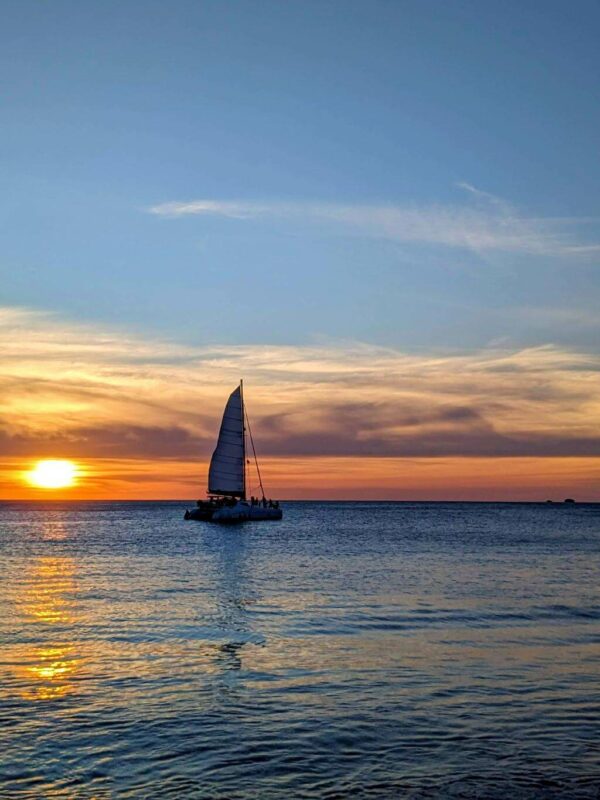 Boat sailing in the blue sea with a sunset painting the sky in warm colors.