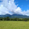 Green pastures at the foothills of the Guanacaste Volcanic Mountain Range with mountains and cloud formations in the background.