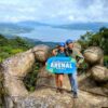 Two travelers posing on La Mano del Arenal, surrounded by lush rainforest with Arenal Lake in the background.