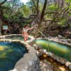 A woman enjoying hot springs in a natural landscape with crystal clear water and trees.