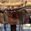 Leather albarda with intricate details and a rolled rope tied to it, used by cowboys for herding and controlling cattle.