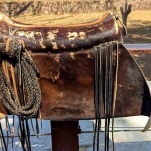 Leather albarda with intricate details and a rolled rope tied to it, used by cowboys for herding and controlling cattle.