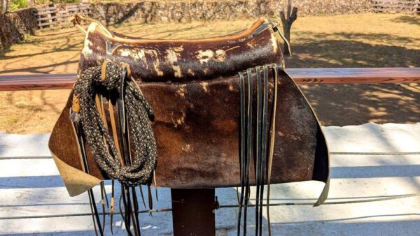 Leather albarda with intricate details and a rolled rope tied to it, used by cowboys for herding and controlling cattle.