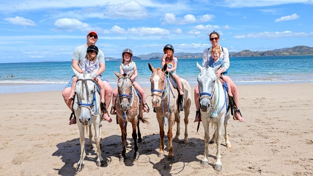 Family wearing helmets posing on horseback with the Pacific Ocean behind them near Conchal Beach in Guanacaste, Costa Rica