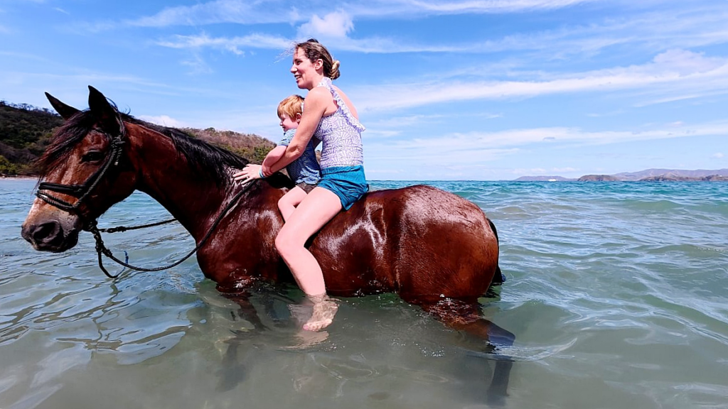 Mother and young child riding a relaxed horse in the ocean after swimming in deeper waters near Conchal Beach, Guanacaste, Costa Rica