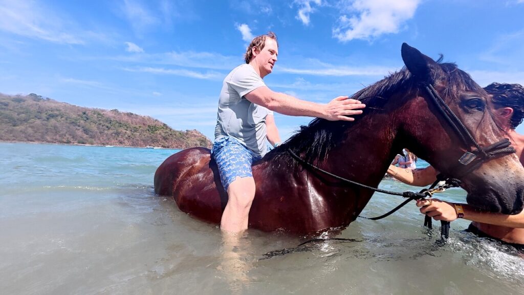 Traveler petting horse while in the ocean during a swimming with horses tour near Conchal Beach in Guanacaste, Costa Rica