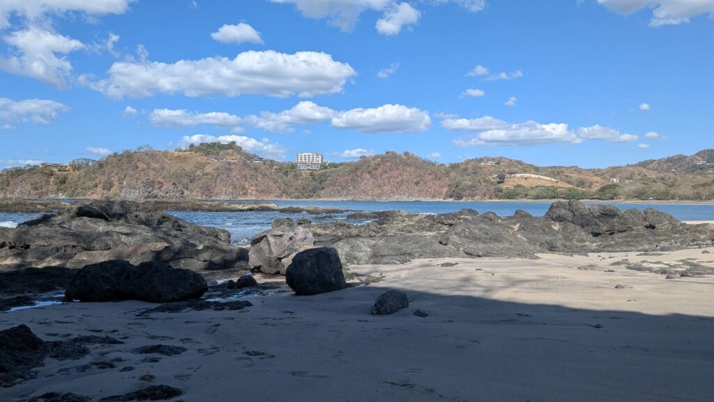 Sunny rocky beach with sand and tide pools under a blue sky with a few white clouds